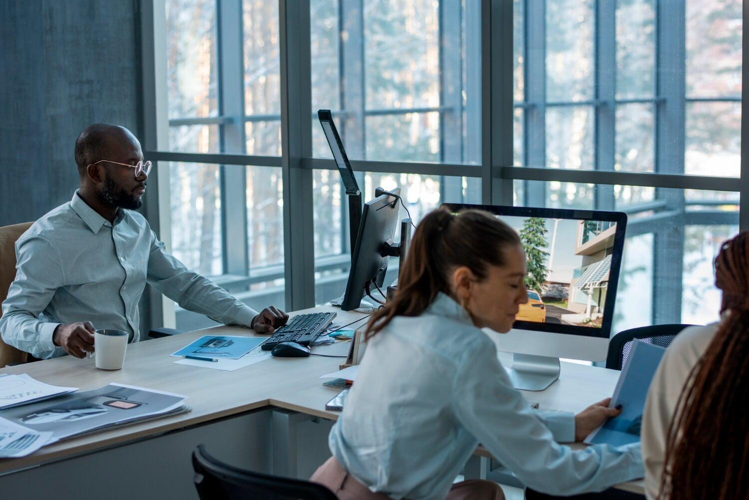 Profissionais trabalhando em escritório com computadores, representando uso de tecnologia no ambiente corporativo